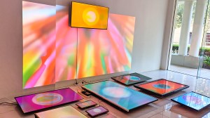 A view of multiple screens showing abstract video in an art installation. Arranged in a grid on the floor, with one one screen on the wall above. They are linked by a luminous projection across the wall.